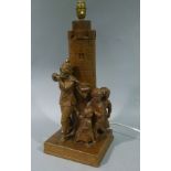 An oak table lamp carved as Pied Piper leading children past a light house, square base,