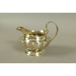 A George IV cream jug of compressed form with fluted body and acanthus cast loop handle,