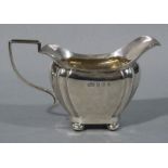 A George V silver cream jug in George III style, angular handle, four compressed bun feet,
