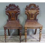 A pair of Victorian mahogany hall chairs with ornate pierced foliate carved waisted backs,