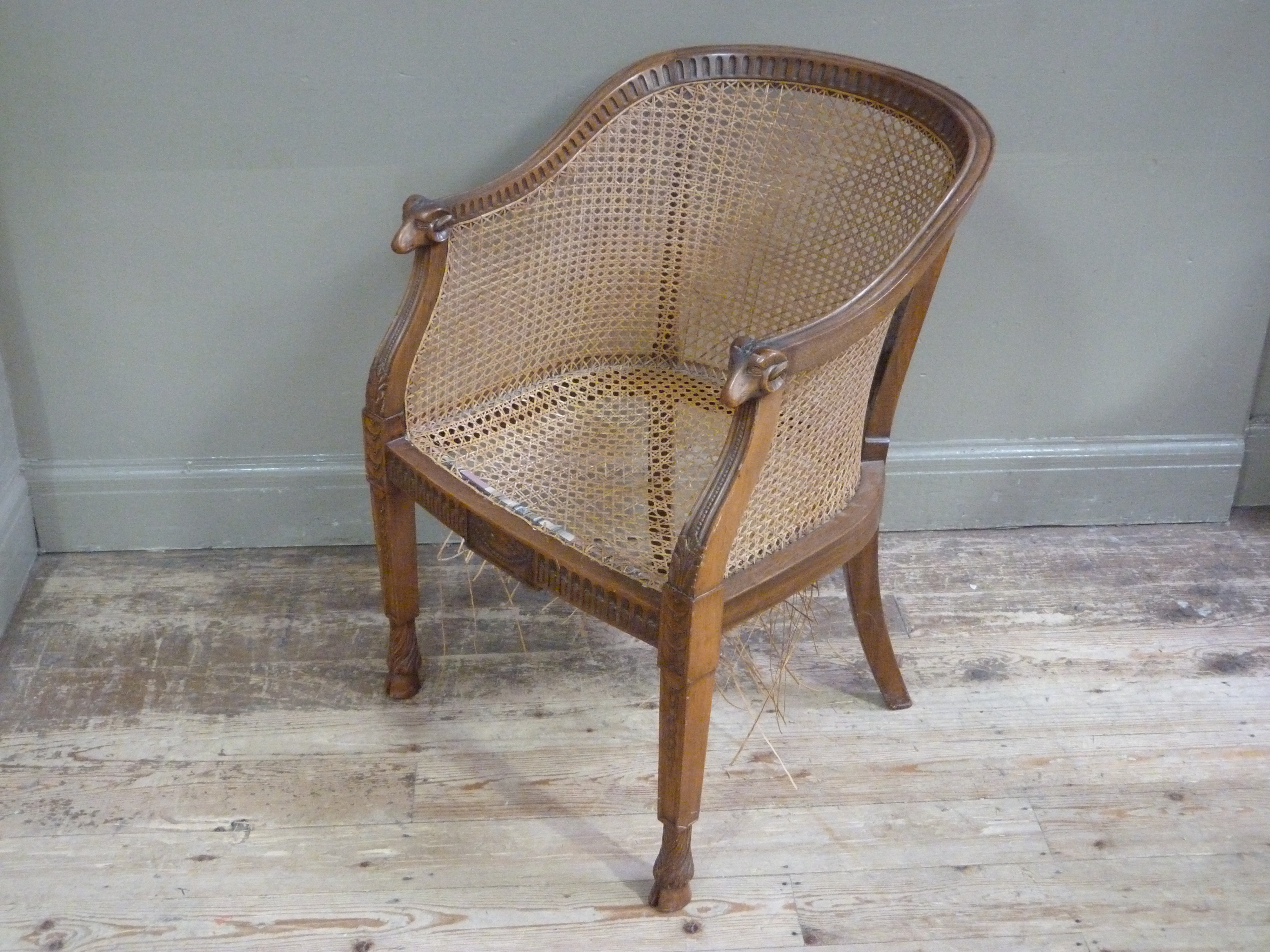 An Edwardian mahogany and bergere caned tub chair the arms with ram mask terminals,