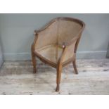 An Edwardian mahogany and bergere caned tub chair the arms with ram mask terminals,