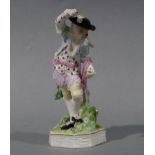An 18th century figure of a man wearing black hat blue jacket with pink waist band standing on a
