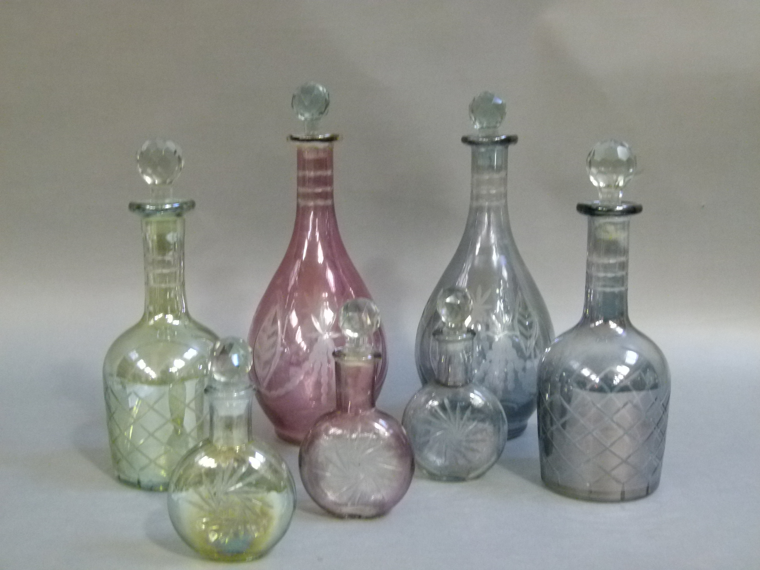 Four coloured glass decanters with faceted globular stoppers; together with a set of three