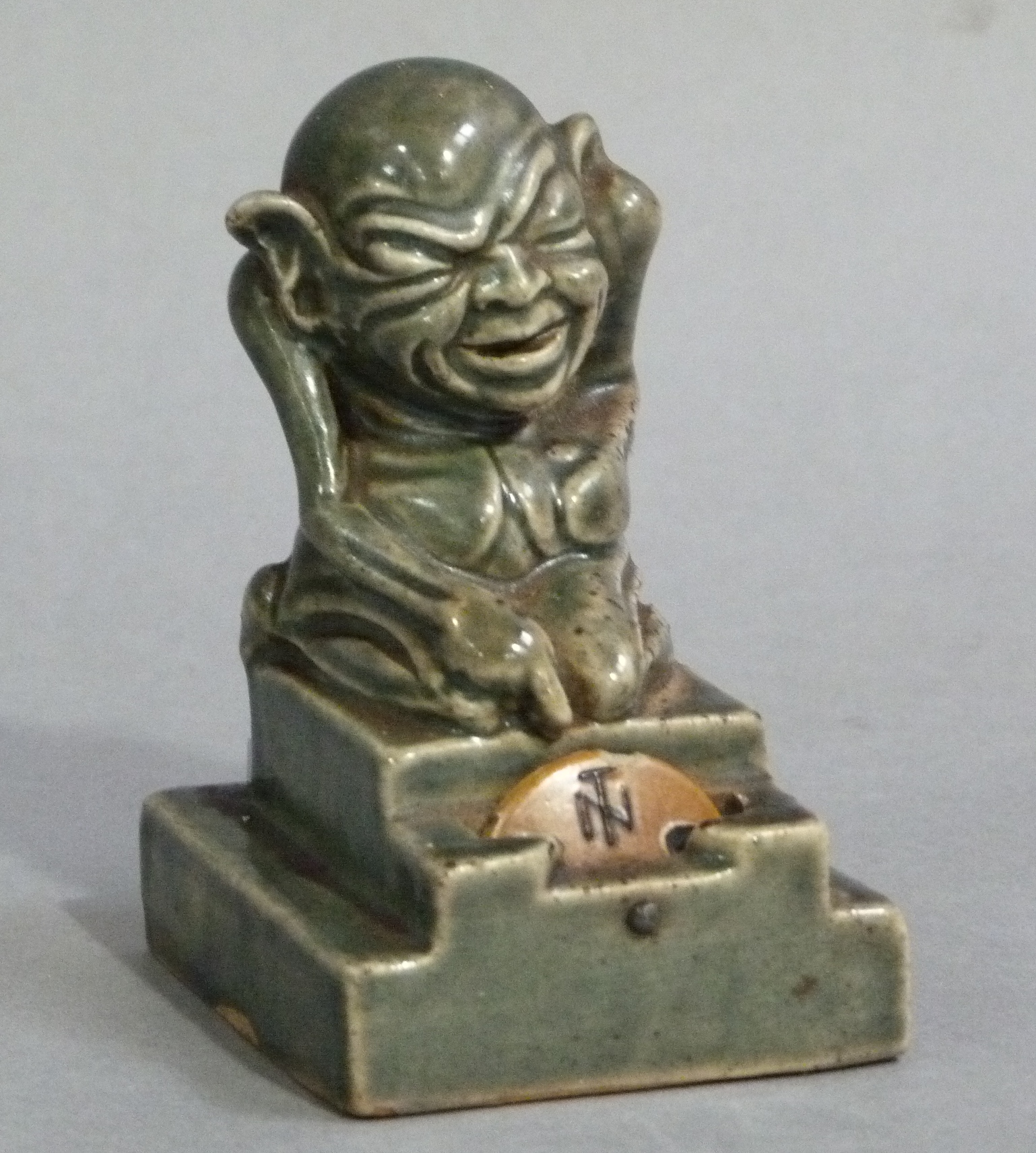 A Doulton Lambeth glazed stoneware card marker an Imp sitting on a stepped plinth pointing to a