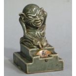 A Doulton Lambeth glazed stoneware card marker an Imp sitting on a stepped plinth pointing to a