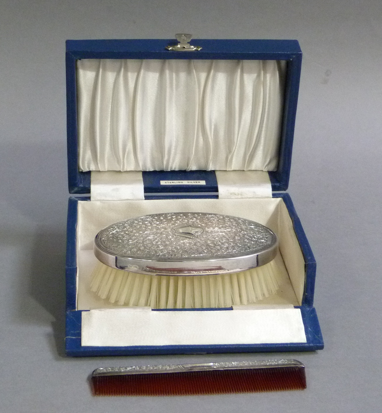 A sterling standard brush and comb set, each piece foliate engraved, the oval brush with vacant