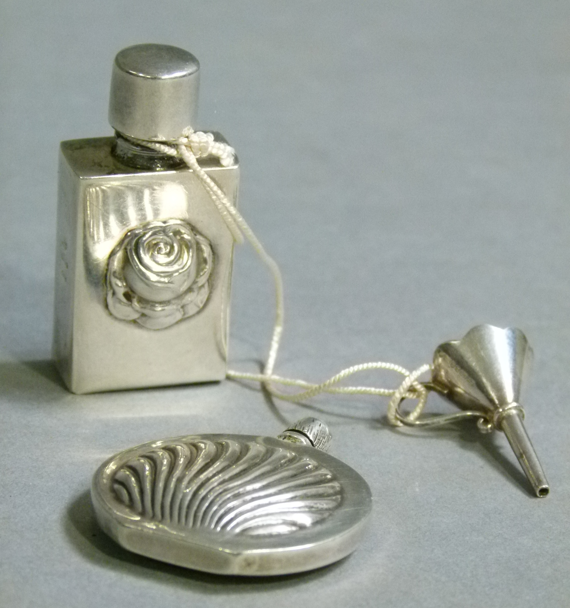 A silver coloured metal spherical flattened scent flask embossed with stylised shell, cylindrical