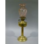 An Edwardian brass oil lamp with associated pink tinted writhen moulded glass shade (no chimney)