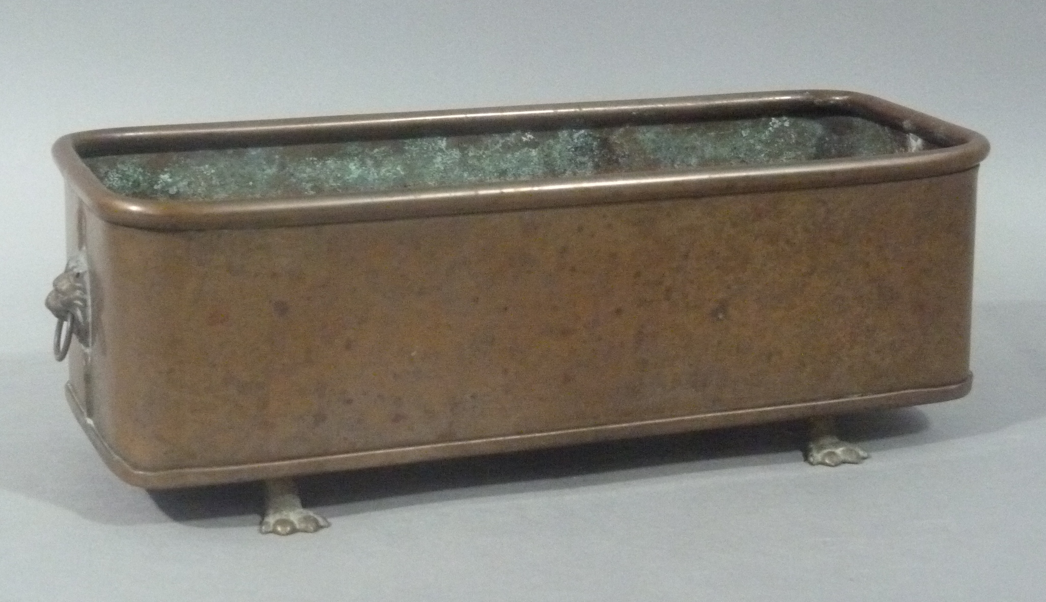 A copper planter with lion mask and ring handles on four brass lion paw feet, 29cm wide