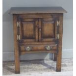 An oak side cabinet having two field panel doors above a drawer on square legs, with h brass