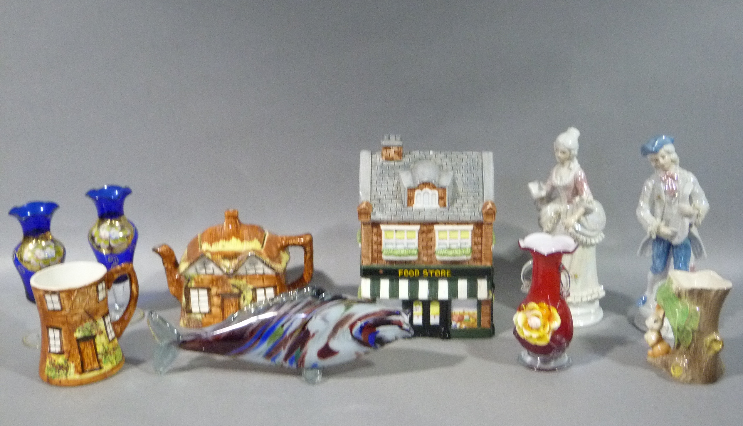 A biscuit barrel in the form of a shop, a marble glass fish, a cottage teapot and mug, Fauna vase,