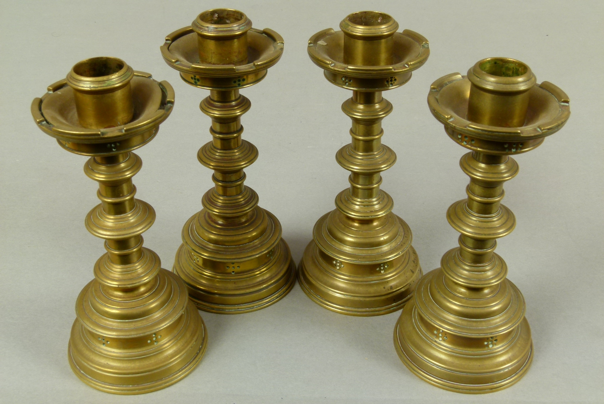 A set of four Victorian brass table candlesticks in the 'Gothic' style, cylindrical nozzles with