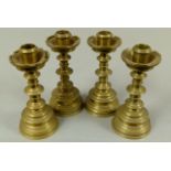 A set of four Victorian brass table candlesticks in the 'Gothic' style, cylindrical nozzles with