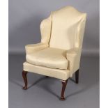 A Queen Anne style mahogany winged armchair, having an arched back and outwardly scrolled arms,