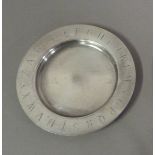 A circular silver dish with shallow dished centre, the border engraved with the alphabet, 16cm