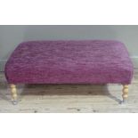 A modern upholstered stool rectangular on pale wood turned legs with chrome caps and castors