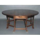 An 18th century style oak double gateleg dining table having twin oval drop leaves, drawer to apron,