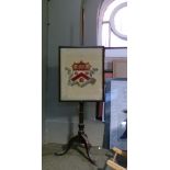 A 19th century mahogany pole screen, having an armorial crest needlework panel and on cabriole legs