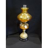 A Circular Based Brass Column Oil Lamp With Amber Tinted Shade