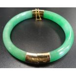 HINGED GREEN JADE BANGLE with fourteen carat gold mounts and safety chain