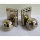 PAIR OF CULINARY CONCEPTS BOOKENDS of cricket balls on shaped oblong bases, in polished steel, boxed