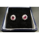 PAIR OF RUBY AND DIAMOND CLUSTER EARRINGS the central ruby on each in twelve diamond surround, in