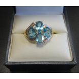 BLUE TOPAZ AND DIAMOND DRESS RING the four oval cut topaz gemstones flanked by decorative split