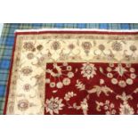 LARGE EASTERN FLOOR RUG with a claret ground decorated with floral motifs encased by a taupe border,
