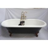 CAST IRON ROLL TOP BATH of oval form and raised on ball and claw feet, with a central brass
