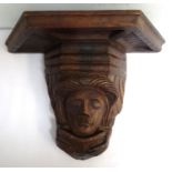 CARVED OAK WALL BRACKET with a shaped top supported by a mask reading a clasped book, 24cm high