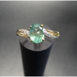 EMERALD AND DIAMOND RING the central oval cut emerald flanked by twist design split shoulders with