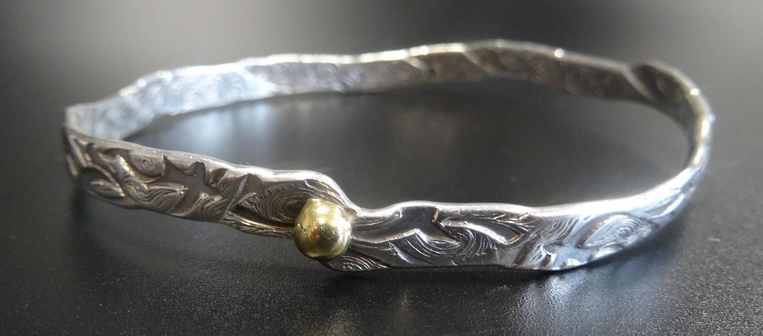 MALCOLM APPLEBY SILVER BANGLE of irregular form with stylised motif decoration overall and gold bead