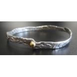 MALCOLM APPLEBY SILVER BANGLE of irregular form with stylised motif decoration overall and gold bead