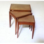 NEST OF THREE TEAK TABLES all with glazed insert tops raised on tapering legs, the widest table,
