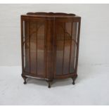 1950s WALNUT BOW FRONT DISPLAY CABINET with a shaped raised back above a pair of glazed doors and