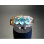 BLUE TOPAZ AND DIAMOND DRESS RING the three graduated oval cut topaz gemstones with illusion set