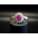 RUBY AND DIAMOND CLUSTER RING the central oval cut ruby in diamond surround and with two diamonds to