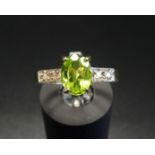 PERIDOT AND DIAMOND RING the central oval cut peridot flanked by two diamonds to each shoulder, on