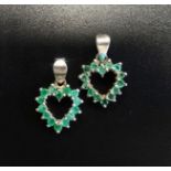 TWO EMERALD SET HEART SHAPED PENDANTS each pendant set with fourteen emeralds, in silver