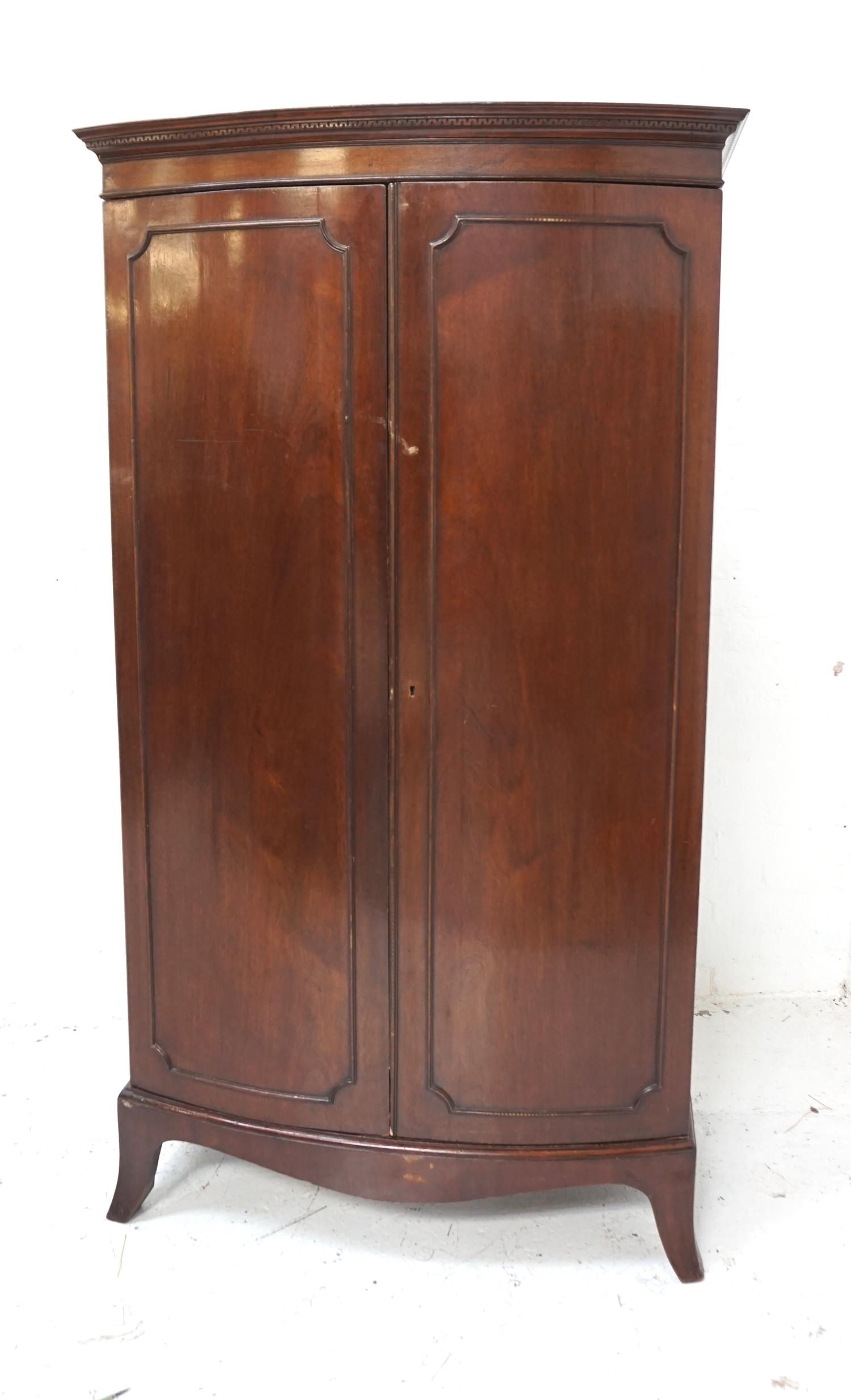 MAHOGANY BOW FRONT WARDROBE with a moulded pediment above a pair of panelled doors opening to reveal