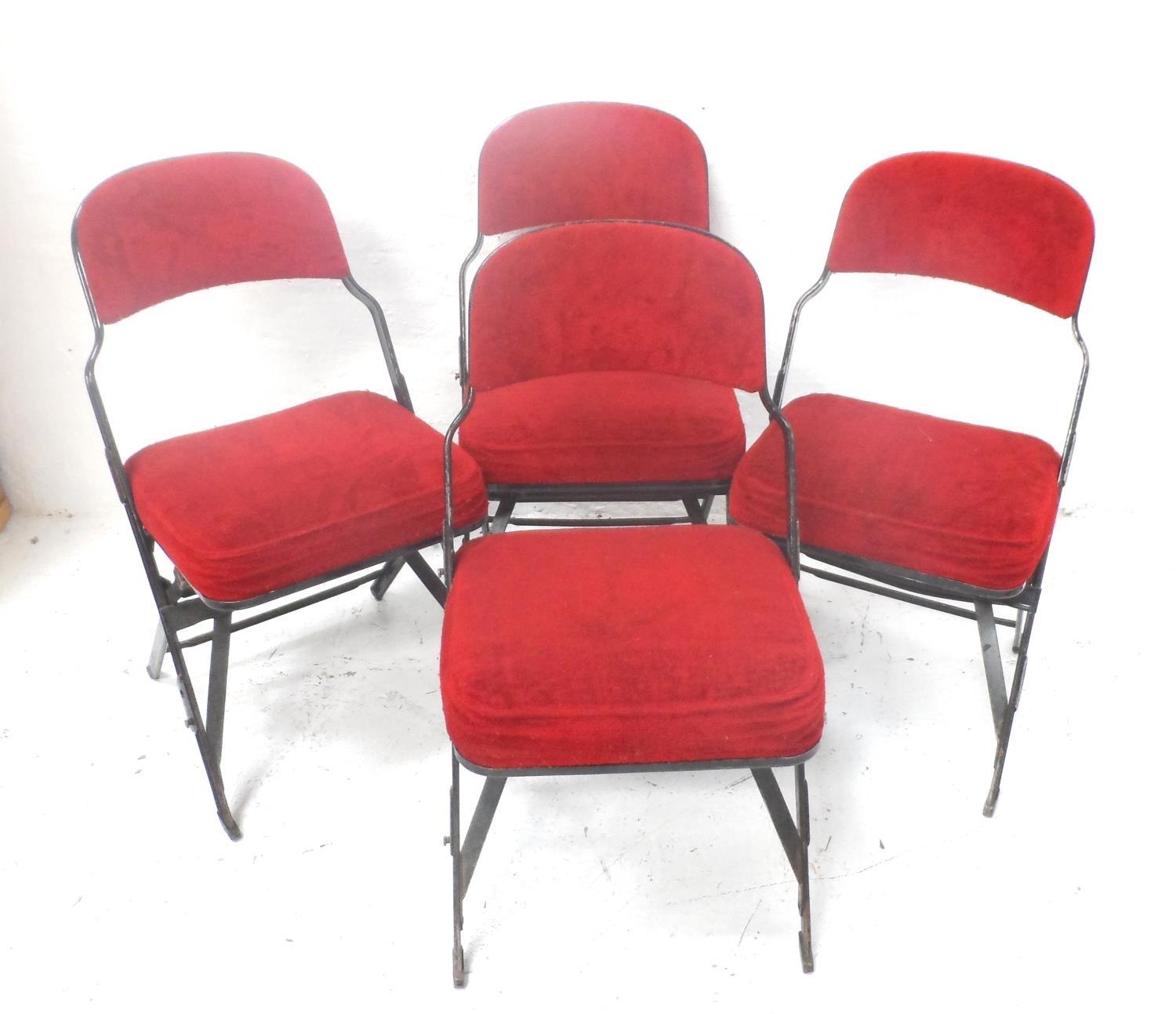 FOUR FOLDING METAL FRAME CHAIRS with shaped backs and padded seats, covered in a plush red