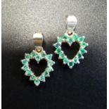 TWO EMERALD SET HEART SHAPED PENDANTS each pendant set with fourteen emeralds, in silver