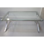 MODERN GLASS TOP OCCASIONAL TABLE with an oblong top on a polished steel base with X frame supports,