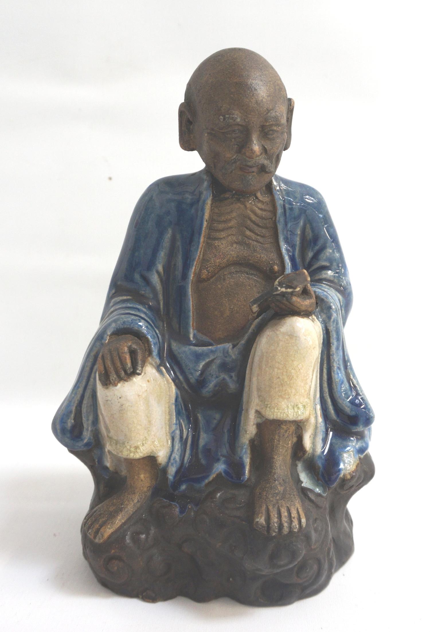 19TH CENTURY CHINESE SHIWAN FIGURE of an old man sat on a rock reading a book and wearing a blue