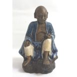 19TH CENTURY CHINESE SHIWAN FIGURE of an old man sat on a rock reading a book and wearing a blue