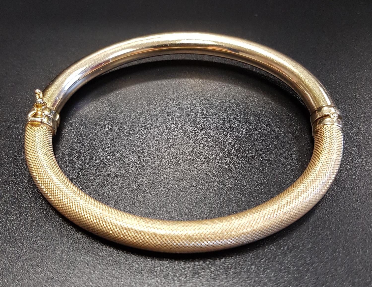 FOURTEEN CARAT GOLD HINGED BANGLE with textured decoration and safety clasp, approximately 10.3