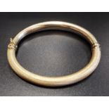 FOURTEEN CARAT GOLD HINGED BANGLE with textured decoration and safety clasp, approximately 10.3