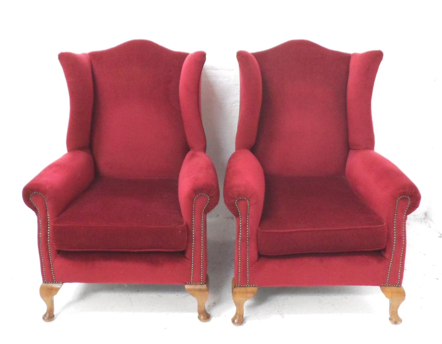 PAIR OF WING BACK ARMCHAIRS with shaped backs, covered in a raspberry coloured velour, standing on