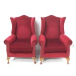 PAIR OF WING BACK ARMCHAIRS with shaped backs, covered in a raspberry coloured velour, standing on